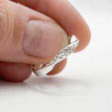 Load image into Gallery viewer, silver ring held in fingertips, held to show almost a top-down view of the ring.
